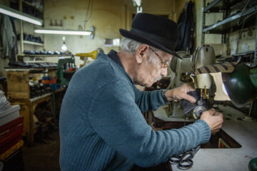 رضا عنایتی ۸۲ ساله ۷۰ سال است که در این حرفه و صنعت فعالیت می کند. او در حال چرخ کاری کفش های کاربری شده است.